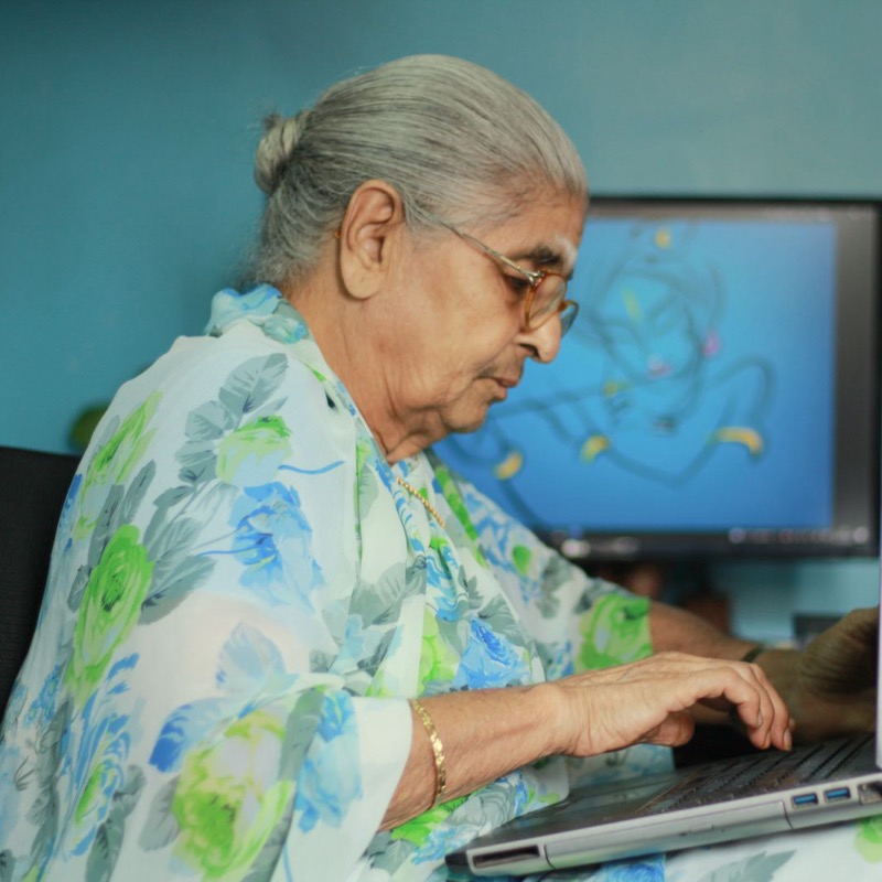 A silver-haired grandmother at home, comfortable on her laptop