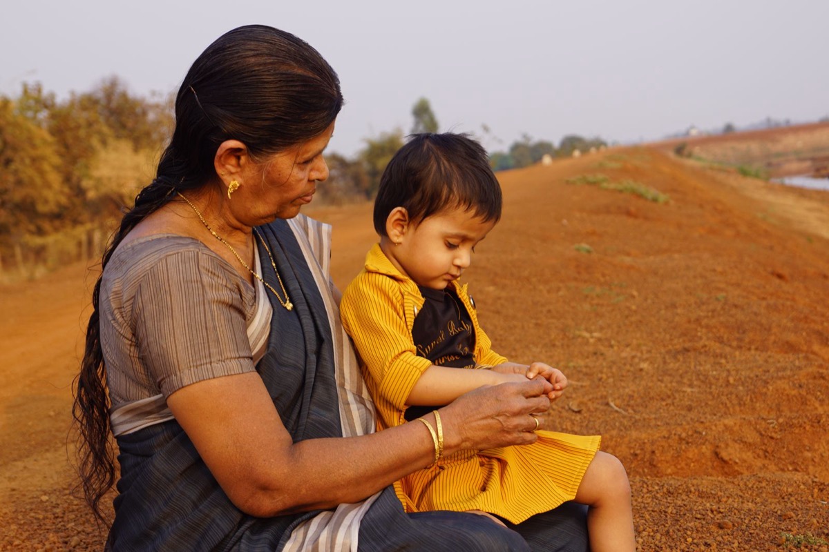 A grandmother and her grandson sitting together on red earth near Raipur